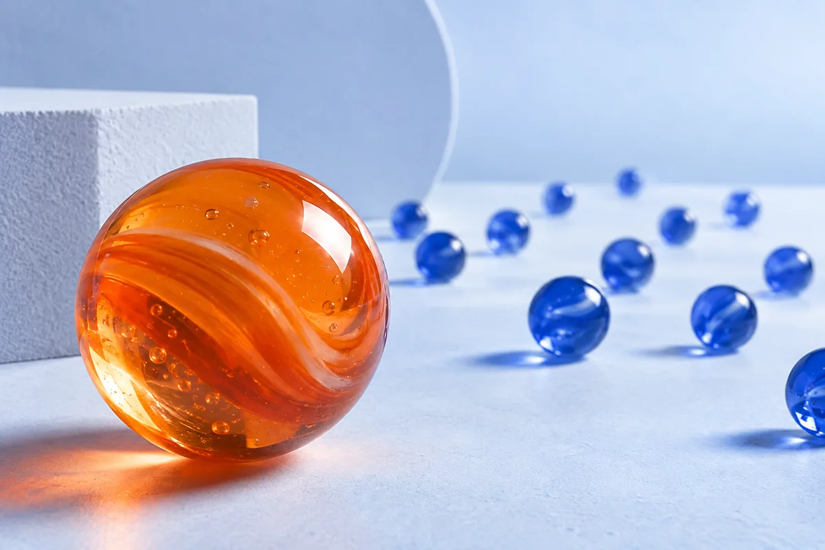 A nearby orange marble and distant blue marbles seen through a lens. AI-created editorial illustration.
